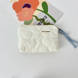 Gros plan sur la trousse matelassée crème avec motifs floraux et cordon tressé bleu
