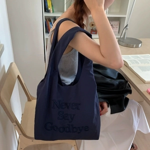 Navy blue nylon tote bag with embroidery detail carried by a model in a cozy room
