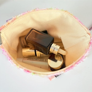 Detail of tweed makeup bag with fringe edge showing large capacity for cosmetics