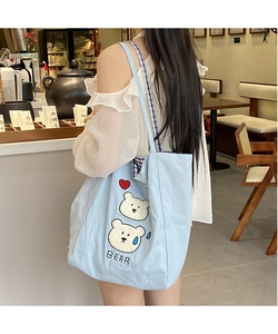 Detail of light blue tote bag featuring cute bear embroidery and blue checkered straps