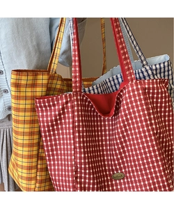 Three oversized plaid canvas tote bags in red, yellow, and blue displayed with handles
