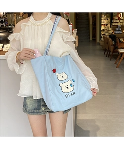 Close-up of blue canvas tote bag featuring bear embroidery and plaid strap details