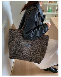 Detail of a large leopard print canvas tote bag with a wide shoulder strap and brand patch