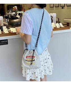 Detail of canvas bucket bag with red BAKERY embroidery and striped shoulder strap