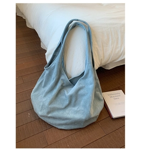 Detail view of large light blue suede tote bag with wide straps on wooden floor