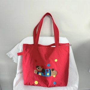Close-up of red nylon tote bag with cartoon dog embroidery and colorful pom-poms