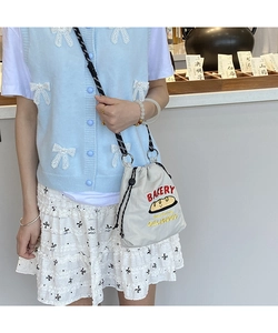 Detail of canvas drawstring bucket bag with bakery print and braided shoulder strap