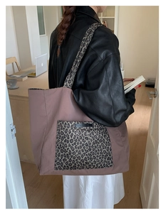Detail view of large leopard print tote bag in rose pink worn by a model in a leather jacket