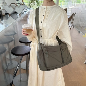 Sac bandoulière en nylon olive porté par une femme dans un café avec une tasse de café