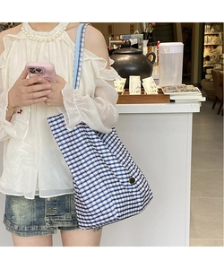 Detail of blue and white checkered canvas tote bag with metal button and shoulder strap
