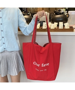 Detail of red canvas tote bag featuring white slogan print and red checkered straps