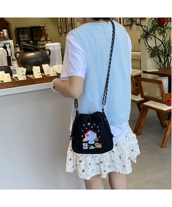 Detail of cartoon embroidery and black-and-white checkered strap on canvas crossbody bag