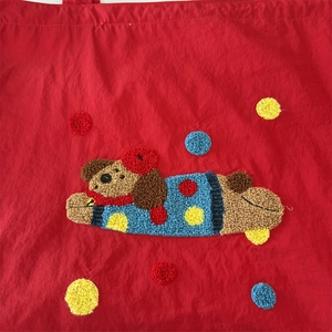 Detail of red nylon tote with textured brown cartoon dog embroidery and colorful dots