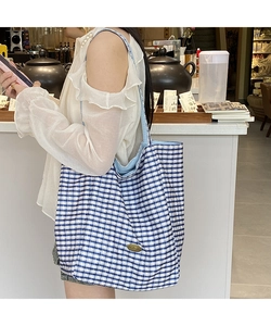 Detail of blue and white checkered tote bag featuring an oval metal logo plaque and soft lining