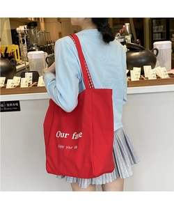 Detail of red canvas tote bag featuring white typography and checkered shoulder straps