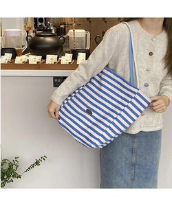 Détail d'un sac cabas en toile à rayures bleues et blanches avec logo en métal et anses