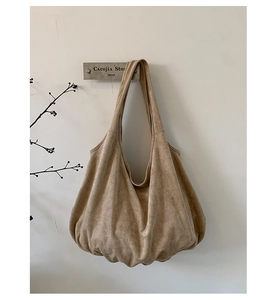 Minimalist camel suede tote bag hanging against a white wall with rustic branch decor
