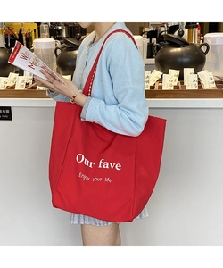 Large red canvas tote bag with white text print worn by model in a casual setting