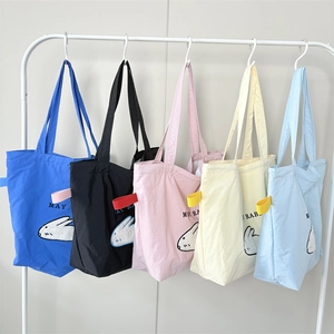 Close-up of five colorful canvas tote bags with rabbit embroidery on white hangers