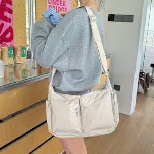 Vue détaillée du sac bandoulière en nylon beige avec doubles poches zippées et sangle réglable