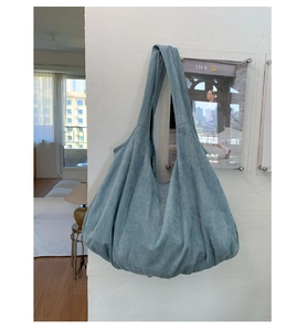 Detail of blue suede hobo tote bag with wide strap hanging on a minimalist white wall