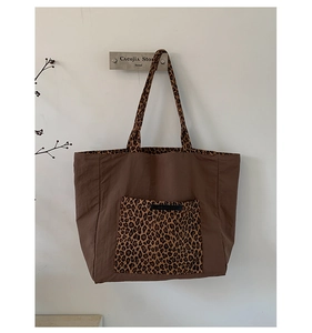 Detail of a large brown nylon tote bag featuring leopard print handles and a front pocket