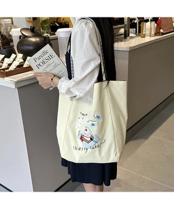 Detailed close-up of beige canvas tote bag with cherry cake embroidery in a cafe setting