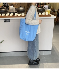 Détail du sac cabas en toile rayée bleu clair avec inscription blanche porté à l'épaule