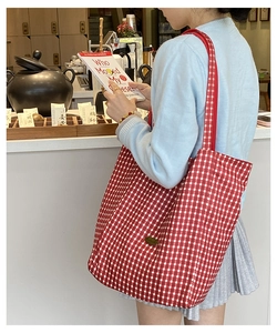 Detail view of large red gingham canvas tote bag with woven shoulder strap on a model