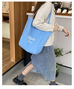 Sac cabas en toile bleu clair avec lettrage blanc présenté dans une boutique chic