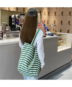 Détail du sac cabas en toile à rayures vertes et blanches avec plaque logo dorée