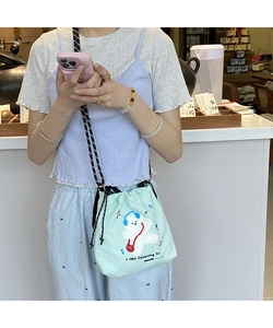 Detail of light green canvas bucket bag featuring a cute teddy bear embroidery and rope strap