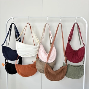 Corduroy crescent crossbody bags displayed in eight solid colors on a white rack