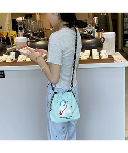 Detail of light blue bucket bag featuring a white bear embroidery and woven shoulder strap