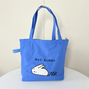 Detail of royal blue canvas tote bag featuring white plush rabbit embroidery and MAY RABBIT text