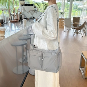 Détail du sac bandoulière en nylon gris à multiples poches porté dans un café lumineux