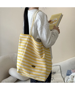 Détail du cabas en toile à rayures jaune et beige avec écusson de logo ovale en cuir