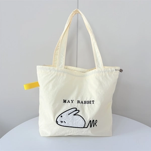 Close-up of cream canvas tote bag with rabbit embroidery and functional drawstring detail