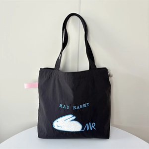 Detail of a black canvas tote bag featuring a white rabbit patch and blue embroidery