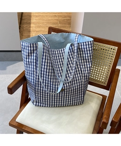 Detail of blue plaid canvas tote bag interior and label on a woven wooden chair
