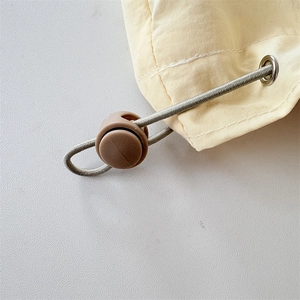 Detailed macro view of plastic cord lock, elastic drawstring, and metal eyelet on yellow fabric