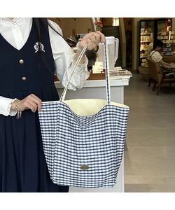 Close-up of blue checkerboard tote bag featuring a handmade metal logo and fabric lining