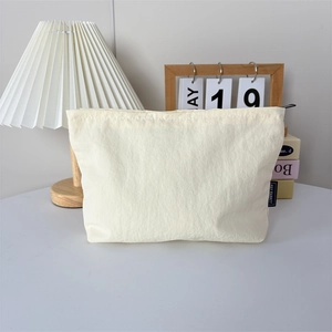 Détail de la trousse de maquillage en nylon crème avec étiquette logo et texture en tissu