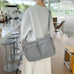Détail d'un sac bandoulière gris en nylon à poches multiples porté par un mannequin