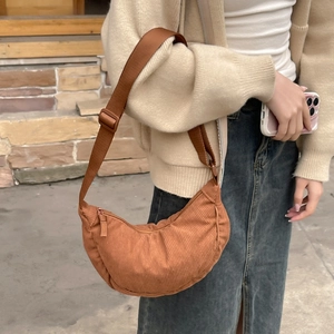 Brown corduroy crossbody half-moon bag worn by model against a natural stone wall