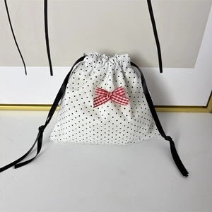 Detailed view of white polka dot drawstring pouch with a red checkered bow decoration