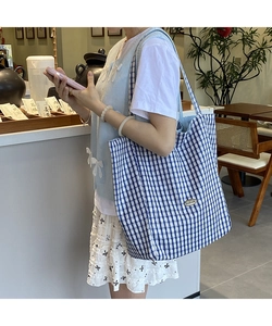 Blue gingham canvas tote bag detail showing the metal logo and spacious side profile