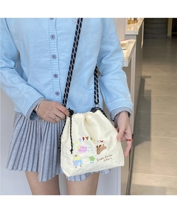 Detail of beige canvas crossbody bag showing colorful puppy embroidery and striped cord strap