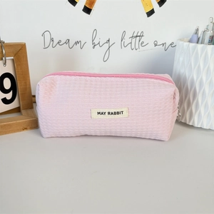 Close-up of pink waffle texture pencil case with brand label and round metal zipper pull