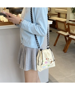 Detail view of beige canvas bucket bag with colorful poppy embroidery and woven rope strap